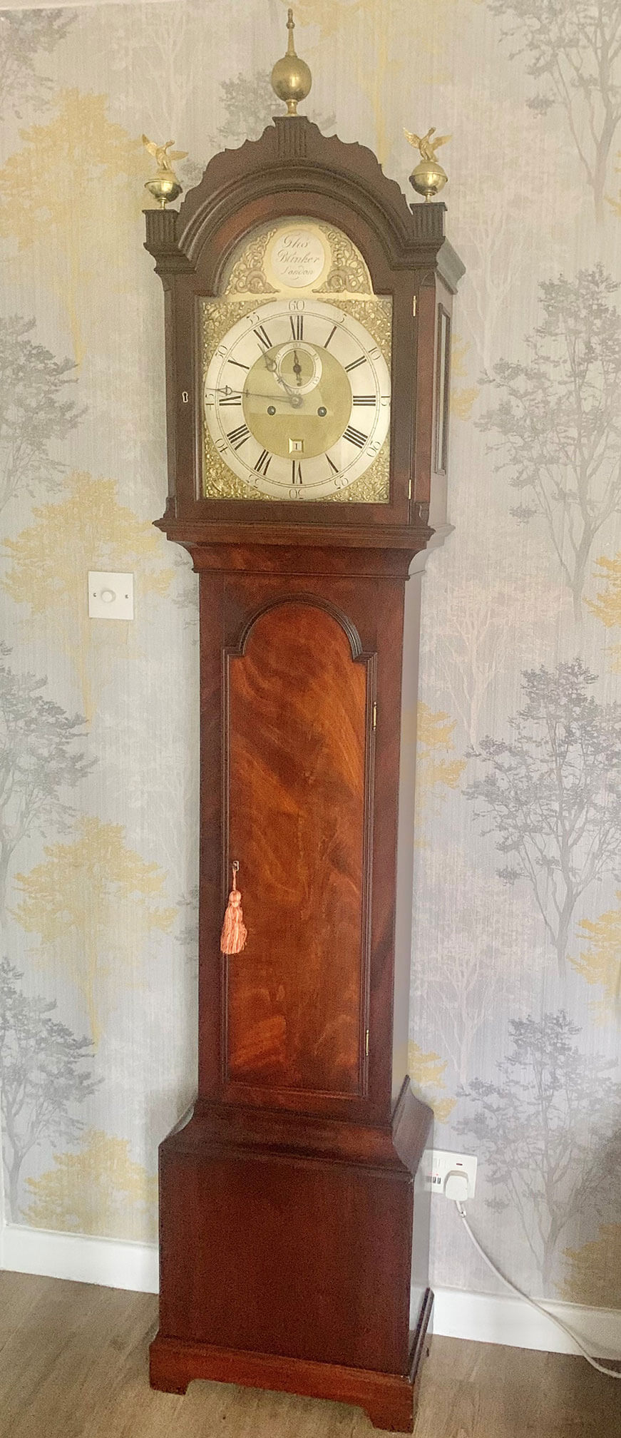 Vintage Wooden Grandfather Clock with Brass Finials Antique wooden grandfather clock with brass finials and a classic clock face, standing tall in a tra.